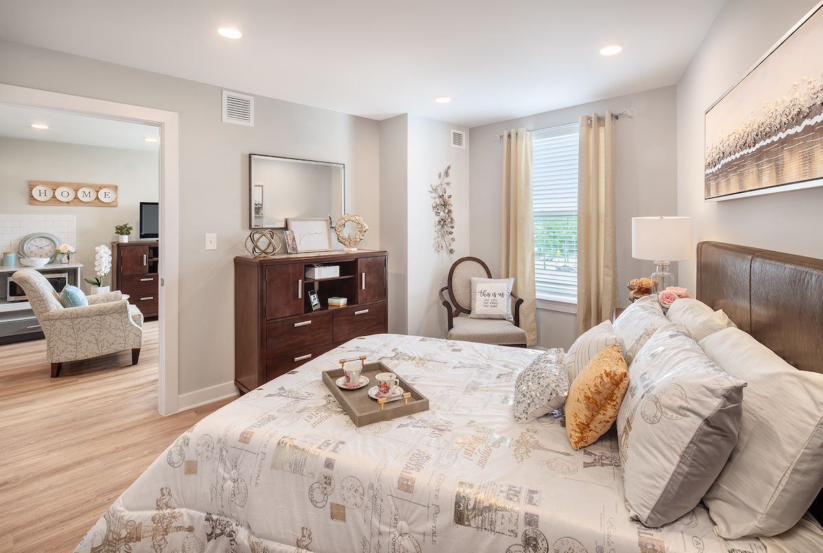 A cozy and well-decorated bedroom with soft bedding, a chest of drawers, and natural light from the window.
