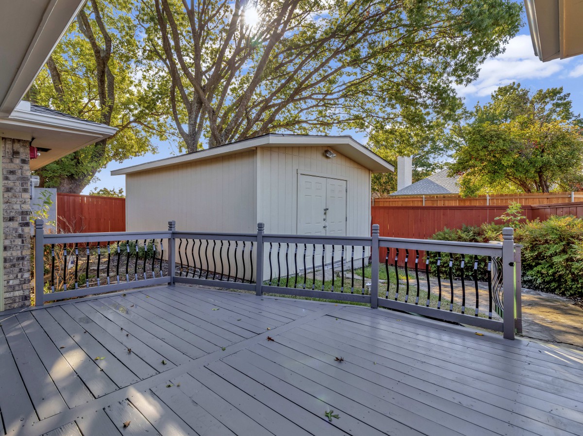 A backyard featuring a wooden deck and a small shed with tall trees in the background.