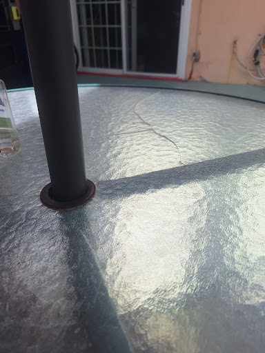 A close-up view of a glass table with reflections and shadows created by an adjacent pole.