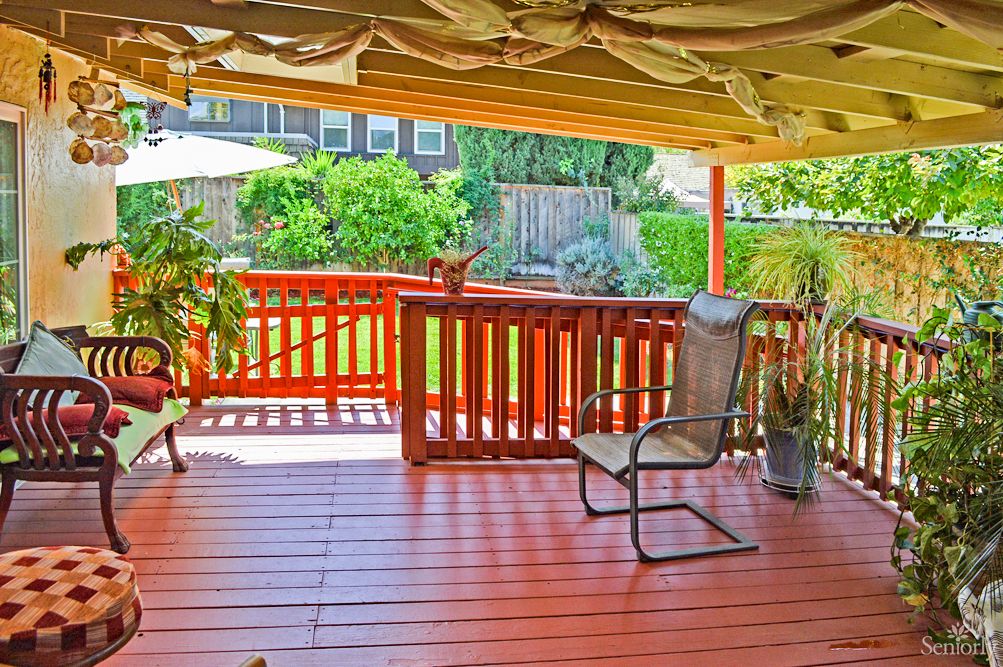 A sunny backyard patio featuring a comfortable chair and wooden deck with surrounding greenery.