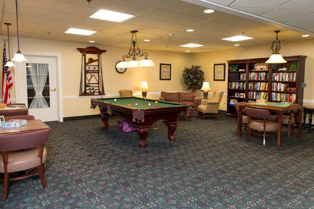 A cozy game room featuring a billiard table and a quiet seating area with bookshelves.