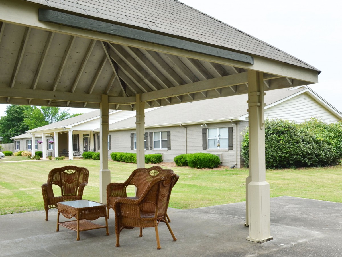 A cozy outdoor gazebo with wicker furniture on a lawn.