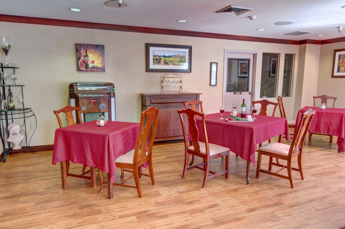 An empty dining area with red tablecloths, wooden chairs, and framed artwork on the walls.