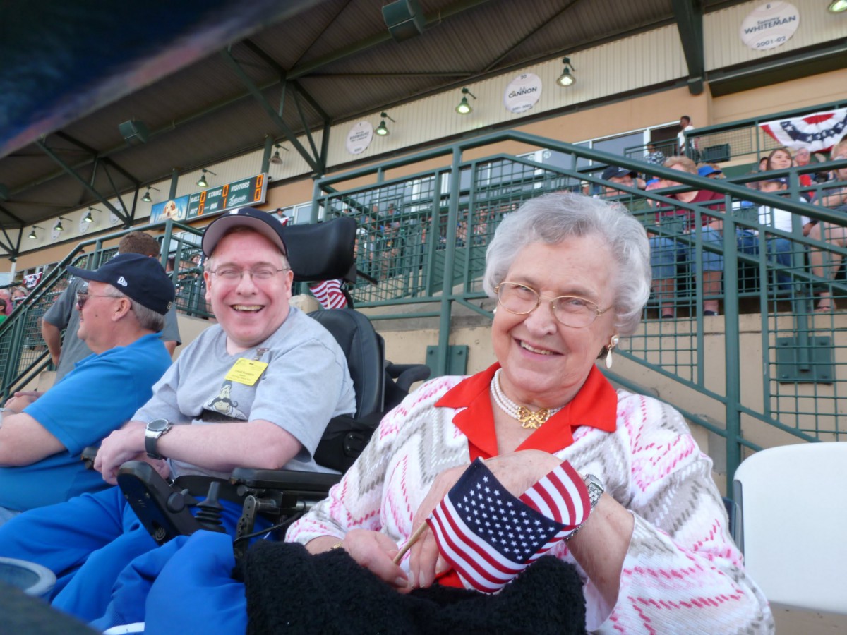 Elderly woman and man at a stadium, smiling and holding an American flag.