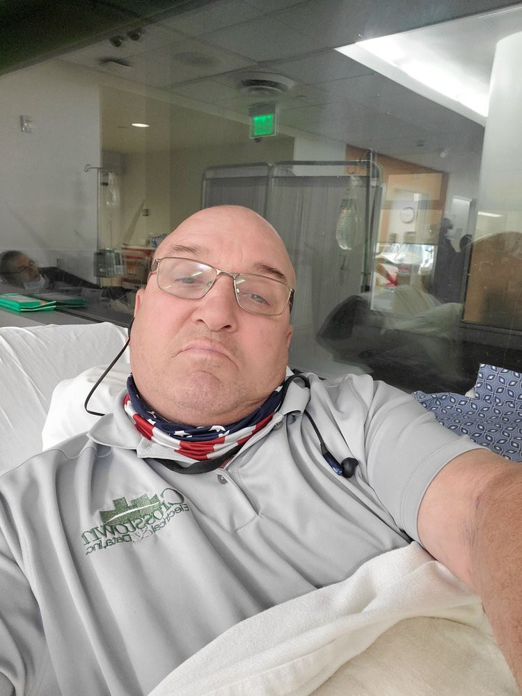 A man wearing glasses and a mask is resting in a hospital setting.