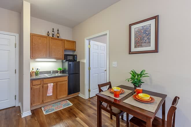 A cozy kitchenette with a small dining area, featuring a fridge, microwave, and wooden cabinets.