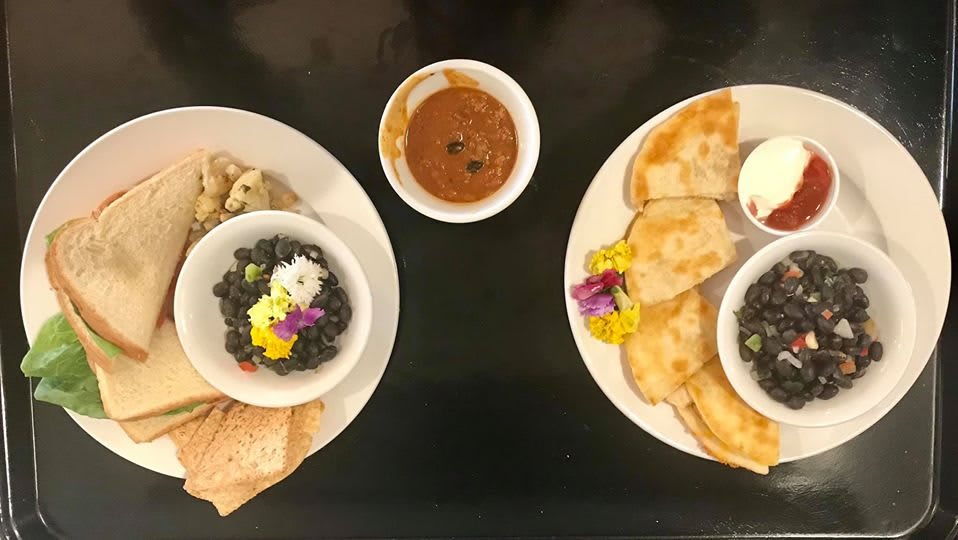 A delightful meal arrangement featuring bowls of black beans garnished with edible flowers, accompanied by bread and a side dish.