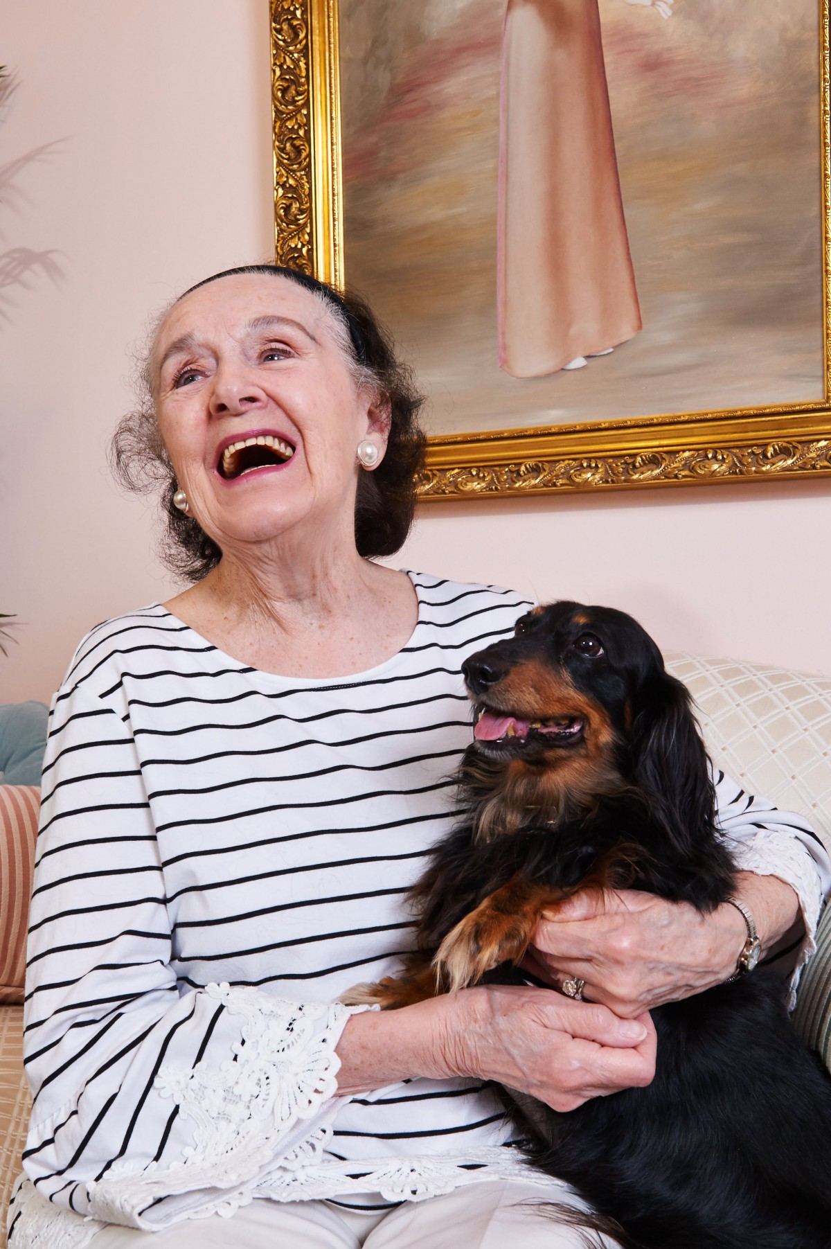 An elderly woman laughing while holding her dog indoors.