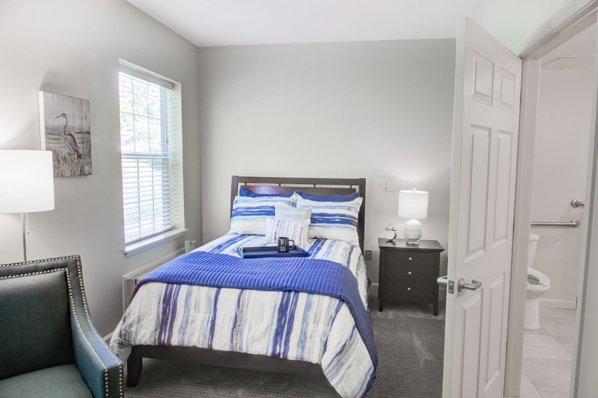 A cozy bedroom with a neatly made bed and a nightstand under soft lighting.