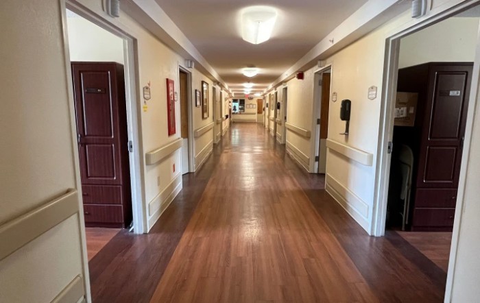 A long, well-lit hallway with wooden floors and doors on either side.