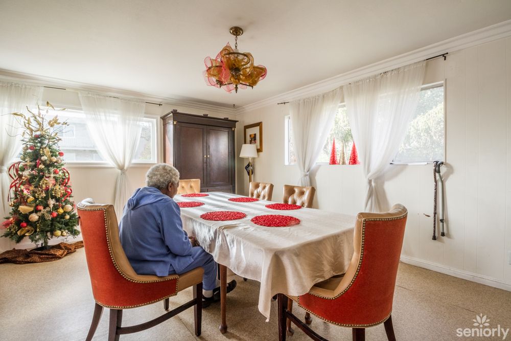 An elderly person sitting alone at a dining table in a well-lit room.