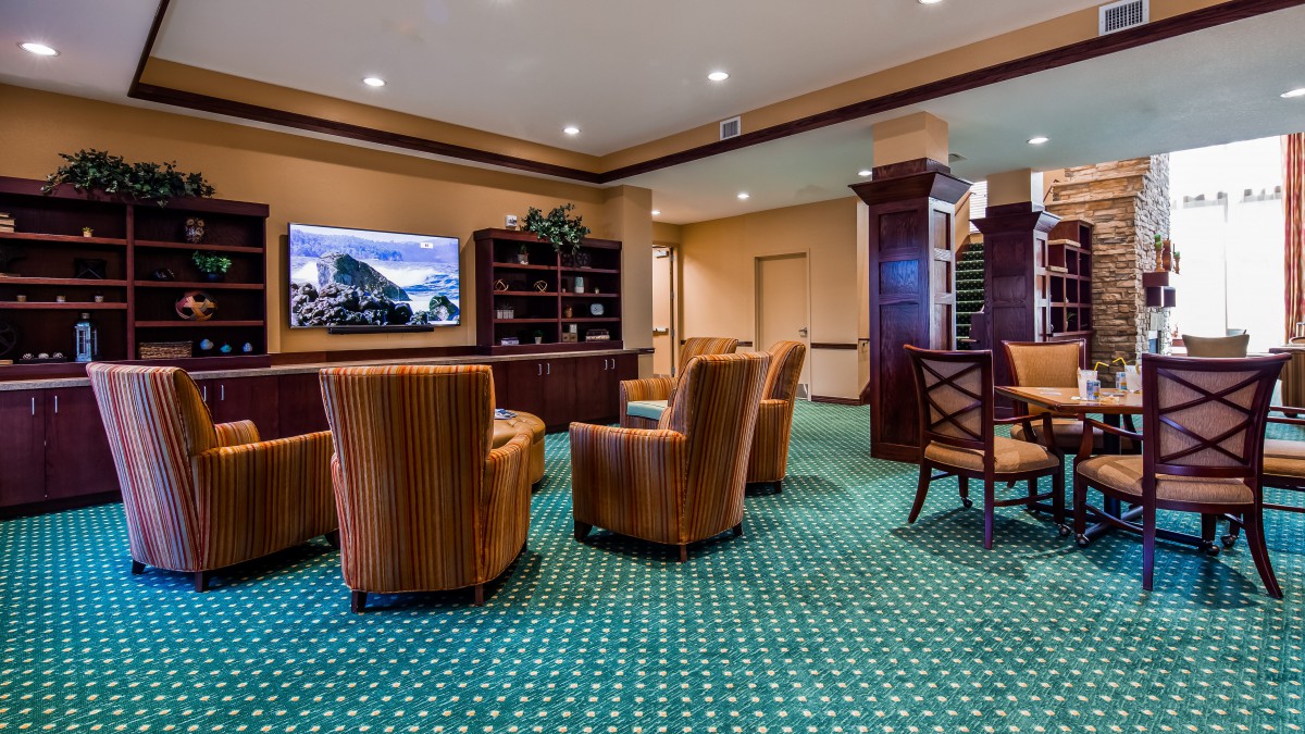A well-furnished lobby area with striped armchairs, a television, and a bookshelf on a patterned carpet.