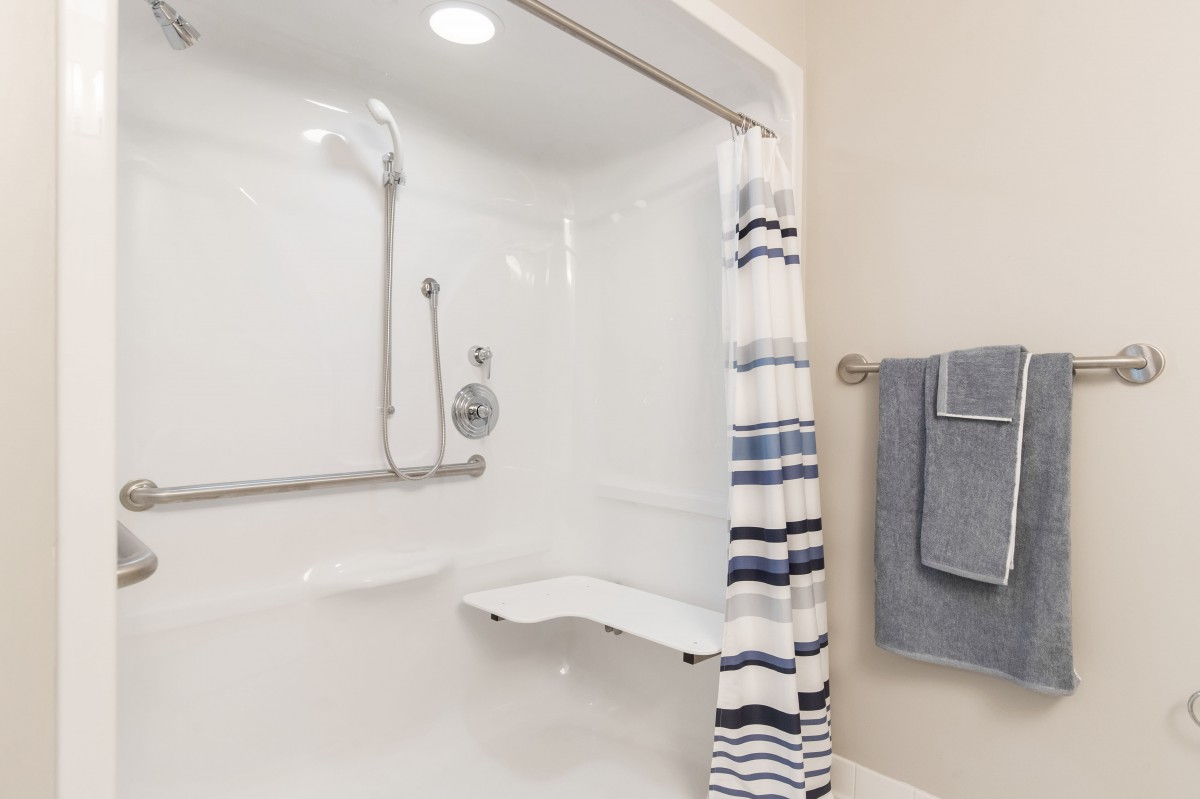 A modern bathroom featuring a shower with a striped curtain, grab bar, and folding seat.