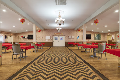A spacious dining area featuring red tablecloths and a stylish chandelier, illuminated by soft overhead lighting.