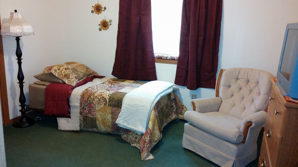 A cozy bedroom with a single bed, floral bedspread, and armchair.