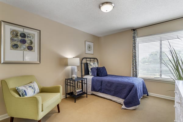 A cozy bedroom with a single bed adorned in blue bedding, an armchair, and large windows letting in natural light.