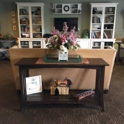 A cozy living room featuring a console table with decorative items and flowers, positioned in front of bookshelves.