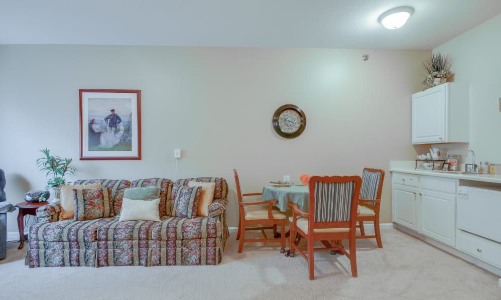 A cozy living room with a striped sofa, dining table and chairs, adorned with wall art and a clock.