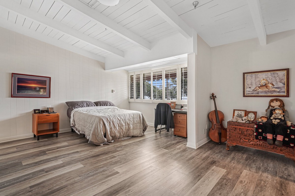 A cozy bedroom with wood flooring, featuring a bed, guitar, and natural light streaming through the window.