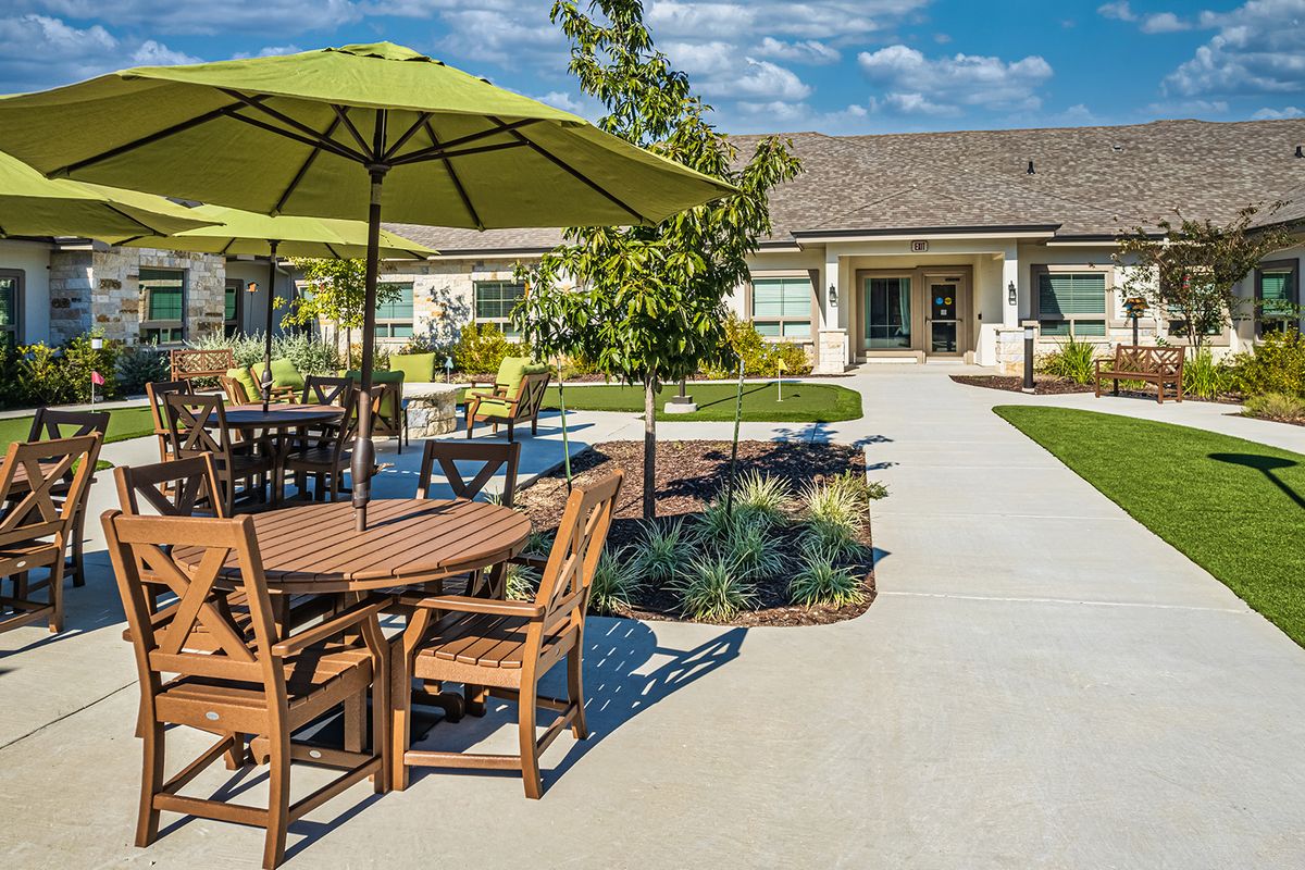 A sunny outdoor patio with tables and umbrellas set in a landscaped garden.