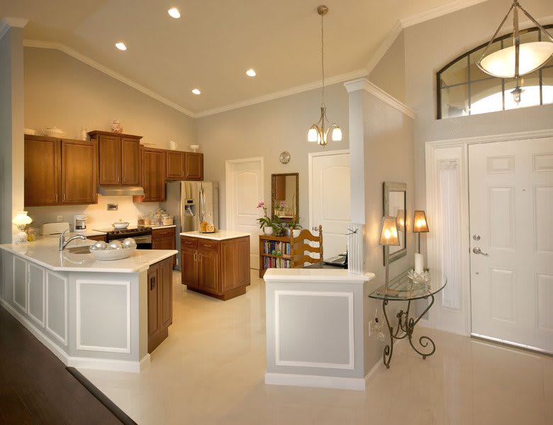 A modern kitchen with wood cabinets and an open dining area, featuring a central island and elegant lighting.