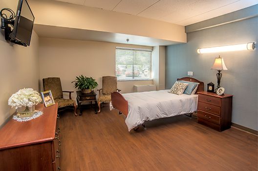 A clean and minimalist hospital room with a bed, chairs, and a window.