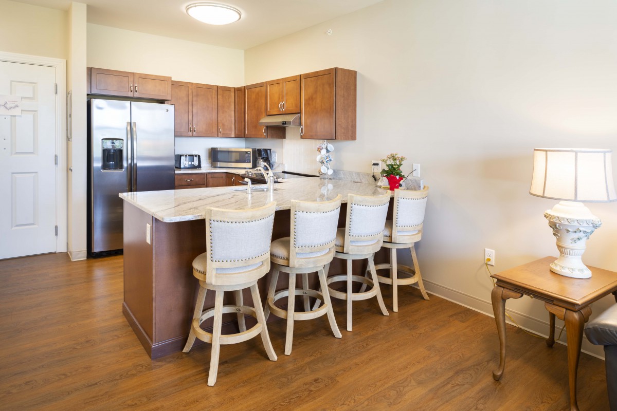 A modern kitchen with wooden cabinets and bar stools along a central countertop.