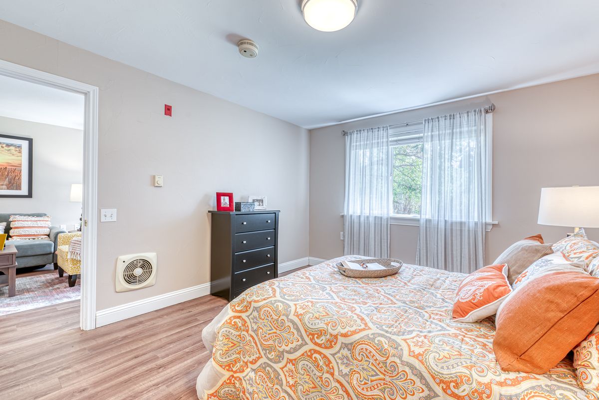 A cozy bedroom with a neatly made bed, dresser, and natural light coming through the window.