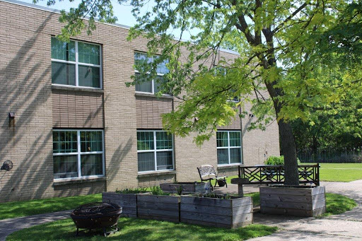 A view of a brick building surrounded by lush greenery and outdoor seating.