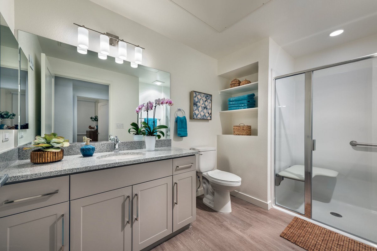 A modern bathroom featuring a vanity with a mirror, a shower, and decorative storage shelves.