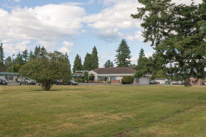 A house surrounded by a large lawn and trees under a cloudy sky.