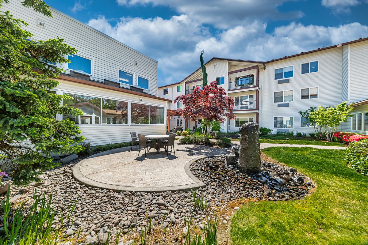 A beautifully landscaped courtyard with outdoor seating, surrounded by a residential building under a blue sky.
