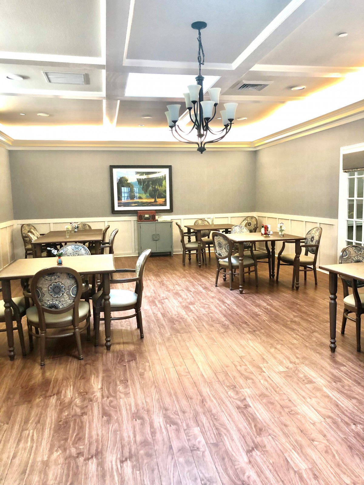 A well-lit dining room with elegant tables and chairs arranged on a wooden floor.
