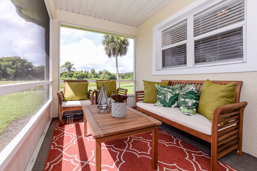 A cozy porch with comfortable seating and green-themed pillows, offering a relaxing view of the outdoors.