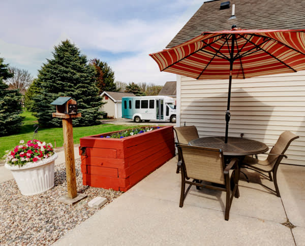 A cozy patio with an umbrella and seating, overlooking a suburban garden with a bus parked in the background.