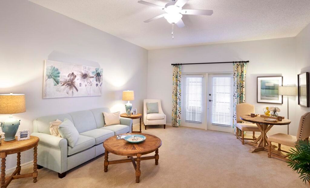 A cozy living room with a sofa, coffee table, and armchairs, featuring a ceiling fan and French doors.