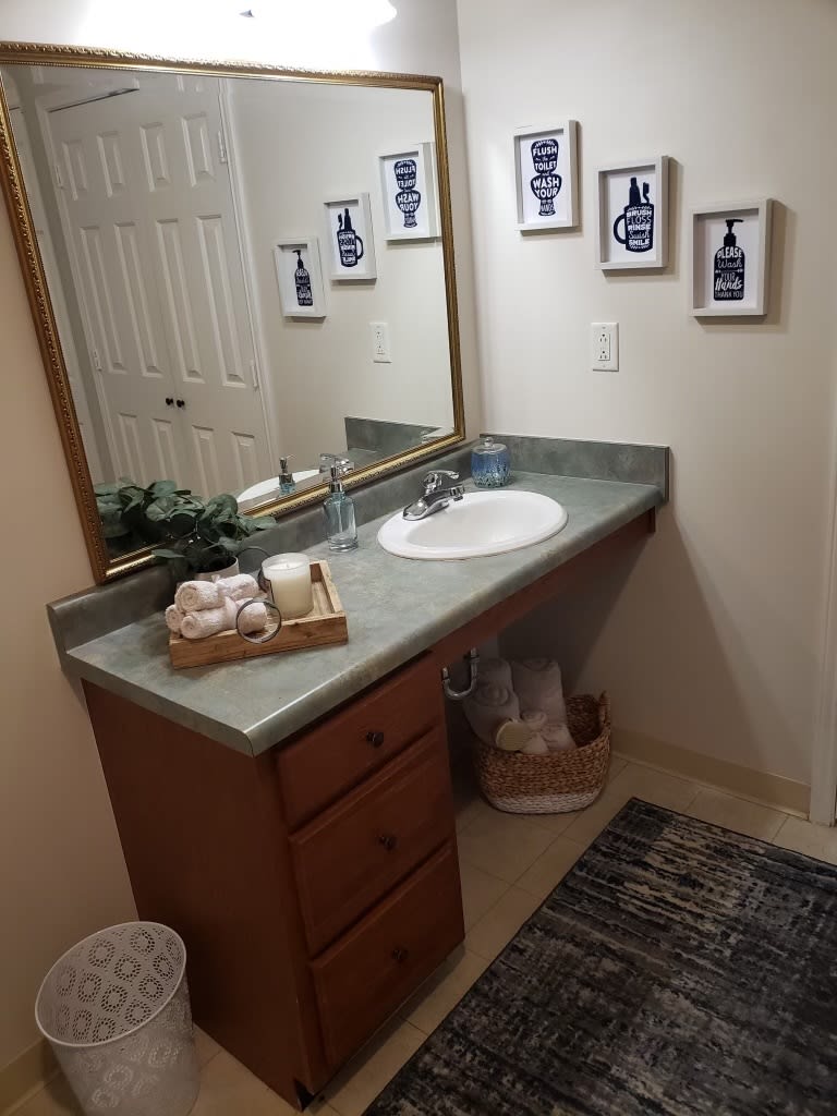 A neatly organized bathroom featuring a sink with a countertop, wall art, and a decorative basket.