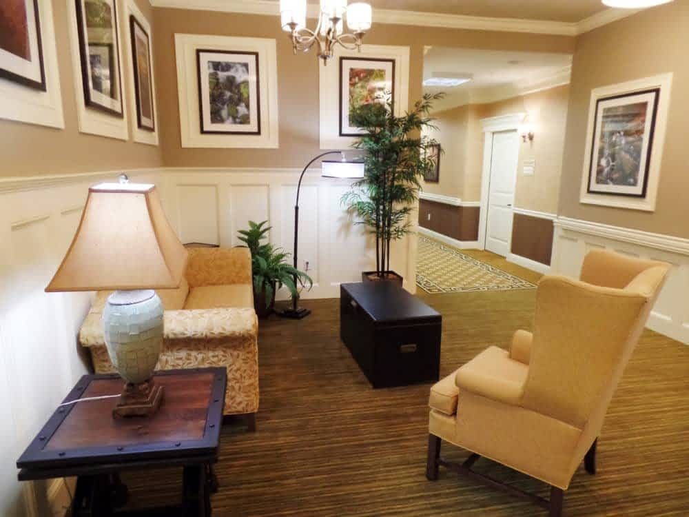 A cozy lobby seating area featuring comfortable chairs, a coffee table, indoor plants, and framed artwork.