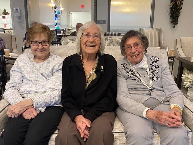 A group of three elderly women sitting together and smiling indoors.