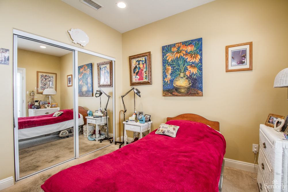 Cozy bedroom with a red blanket, decorated with artwork and mirrored closet doors.