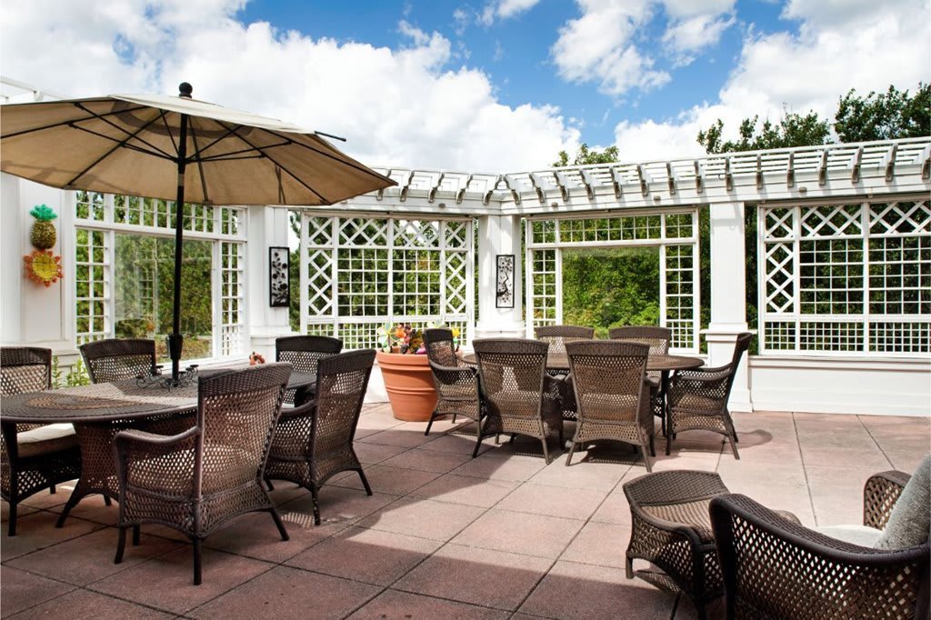 A sunny outdoor patio with wicker chairs and tables under a pergola.