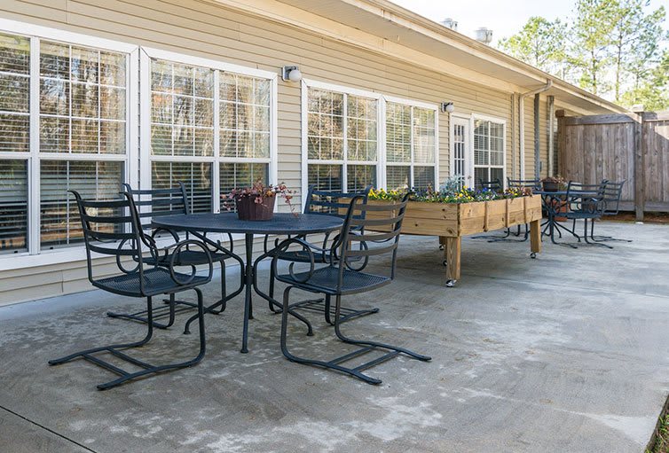 A patio with metal chairs and tables, adjacent to a building with large windows and planters.