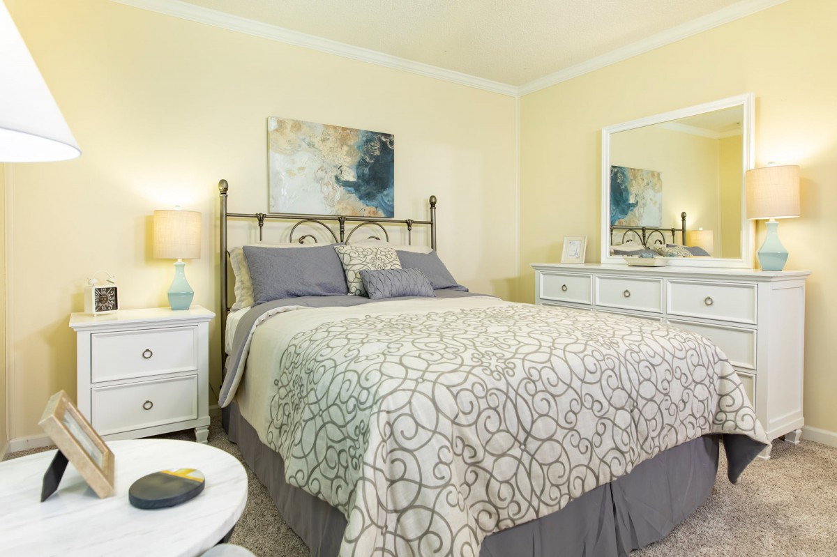 A cozy bedroom with a well-decorated bed, nightstand, and dresser featuring a mirror.
