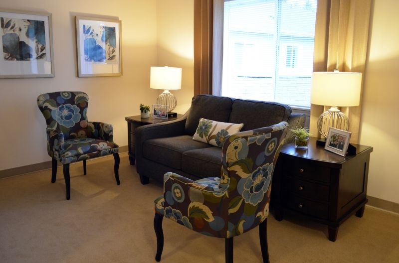 A cozy living room with a dark sofa, patterned armchairs, and warm lighting.