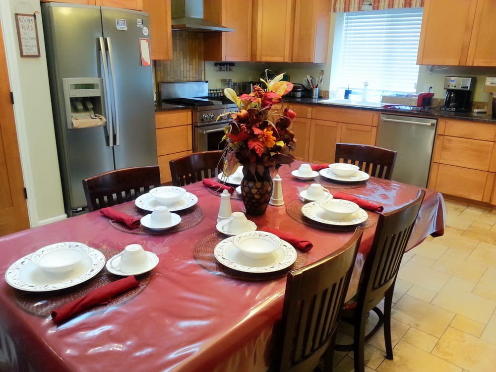 A kitchen with a dining table set for a meal, featuring a floral centerpiece and neatly arranged tableware.