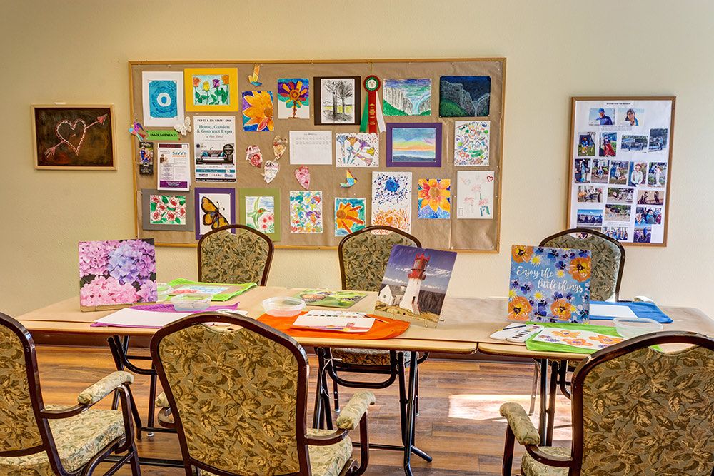 A classroom setting with tables and chairs, featuring a bulletin board displaying various artworks.