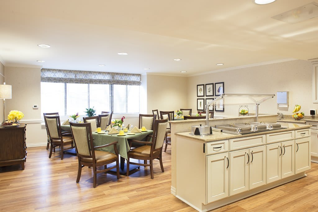 A modern dining room with a kitchen area featuring elegant tables and chairs on wood flooring.