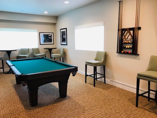 A cozy billiard room featuring a pool table, chairs, and cue rack.