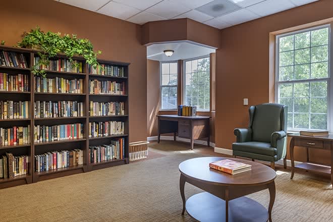A cozy reading area in a library with bookshelves, an armchair, and a window letting in natural light.