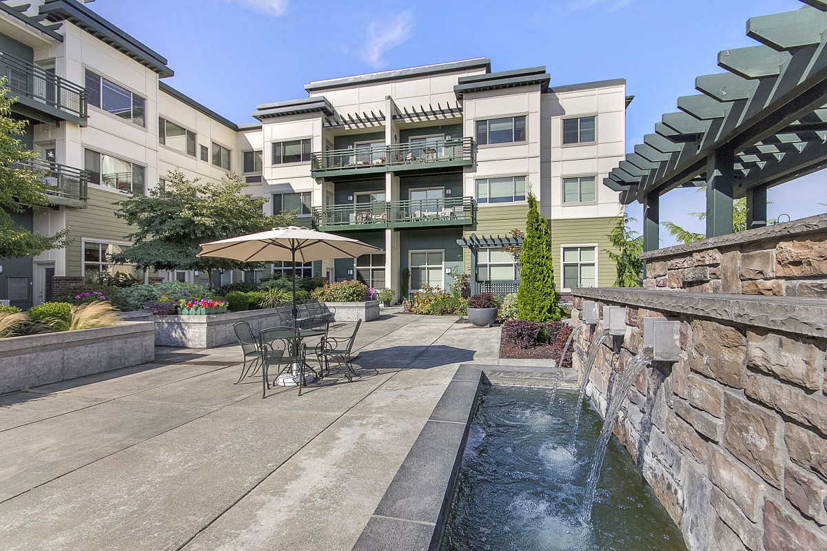 A modern apartment building with an outdoor area featuring a fountain and patio furniture.